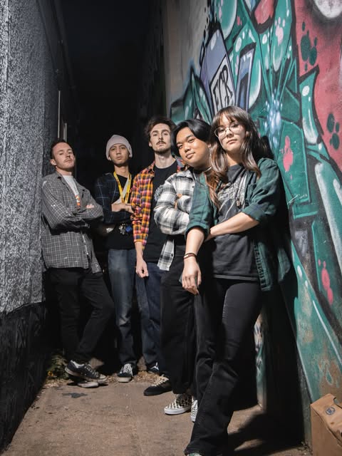 Group portrait beside a graffiti-covered wall.